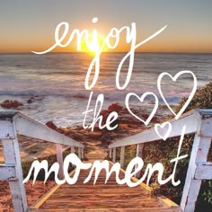 a wooden walkway leading to the ocean with words saying enjoy the moment