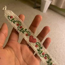 a hand is holding a piece of beaded fabric with flowers and leaves on it