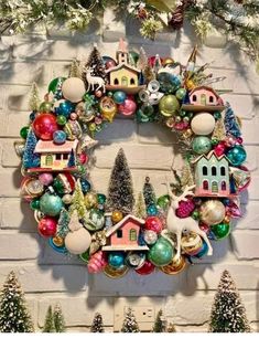 a christmas wreath hanging on the side of a brick wall with ornaments and trees around it