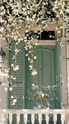 a green door with white flowers growing over it and a light fixture on the side