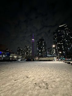 the city skyline is lit up at night, with snow on the ground and buildings in the background