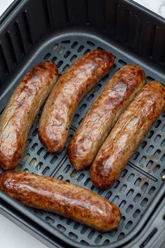 four sausages are being cooked on a grill in an air fryer with tongs