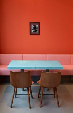 a blue table and two brown chairs in front of a red wall with pictures on it