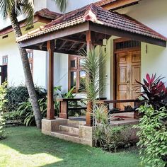 a house that is in the grass with trees and bushes around it, next to some plants