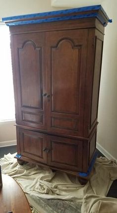 a wooden armoire sitting on top of a pile of cloth next to a window