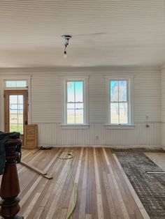 an empty living room with hard wood flooring and two windows on the far wall