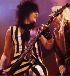 two women with black and white hair are playing guitars on stage together, one is holding an electric guitar