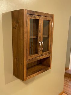 a wooden cabinet with glass doors on the front and bottom, mounted to a wall