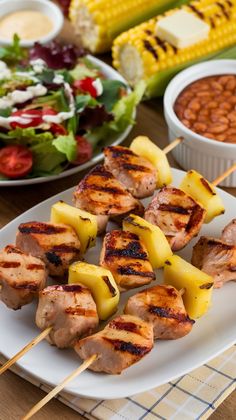 grilled chicken and pineapple skewers on a white plate next to salad