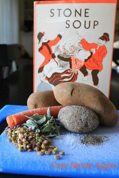 a blue cutting board topped with rocks and vegetables next to a book about stone soup