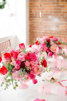 the table is set with pink and red flowers in vases, candles, and plates