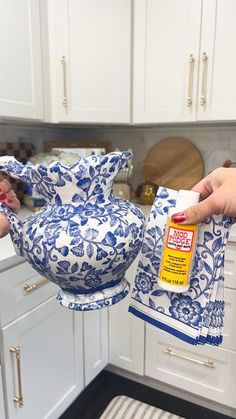 a woman is holding a blue and white vase in the kitchen while cleaning it with a rag