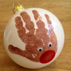 a handprinted ornament on top of a wooden table with a red nose