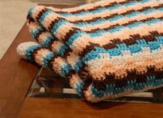 a crocheted blanket sitting on top of a wooden table next to a chair