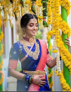 a woman in a blue and pink sari standing next to some yellow garlands