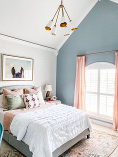 a bedroom with blue walls, white bedding and pink drapes on the windowsill