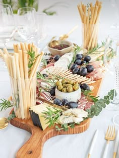 an assortment of cheeses, olives and bread sticks on a wooden platter