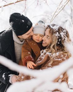 a man and woman holding a small child in their arms while they are covered with snow