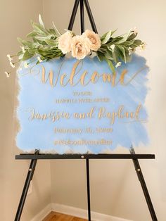 a welcome sign with flowers and greenery on it