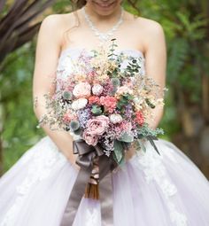 a woman in a wedding dress holding a bridal bouquet with pink and purple flowers