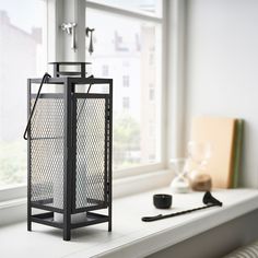 a black metal cage sitting on top of a window sill next to a cup