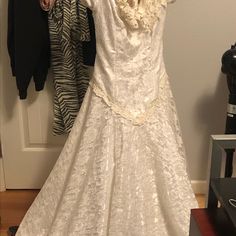 a white wedding dress hanging on a rack in front of a door with other clothes