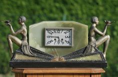 a clock with two women sitting on it's sides and holding hands in the air