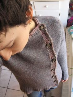 a young boy wearing a sweater with buttons on the front and back, standing next to a stove