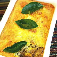 a casserole dish with meat, cheese and green leaves on the top is ready to be eaten