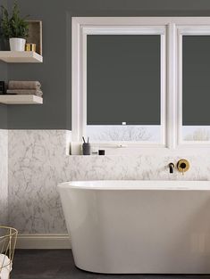 a white bath tub sitting next to two windows in a bathroom with gray walls and flooring