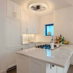 a kitchen with white cabinets and an island in the middle is lit by a ceiling fan