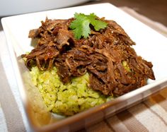 a white plate topped with meat and rice covered in green garnish on top of a table