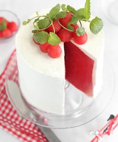 a white cake with strawberries on top is sitting on a red and white checkered tablecloth