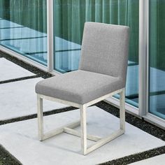 a gray chair sitting on top of a white floor next to a glass wall in front of a building