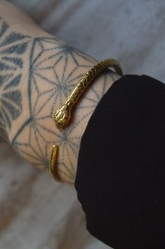 a person with tattoos on their arm wearing a gold snake bracelet and ring, while holding onto the wrist