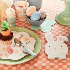 a table topped with plates filled with cupcakes and bunny decorations on top of a checkered table cloth