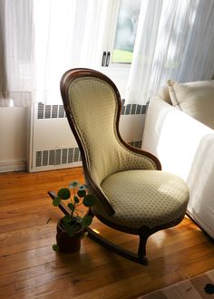 a chair sitting on top of a hard wood floor next to a window with white curtains