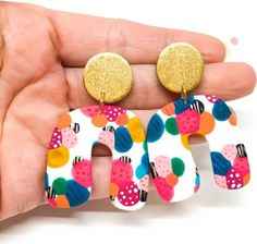 a pair of colorful earrings that are on someone's left hand in front of a white background