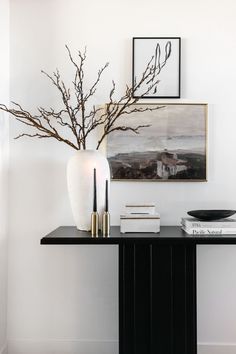 there is a vase with some branches in it on the table next to books and pictures