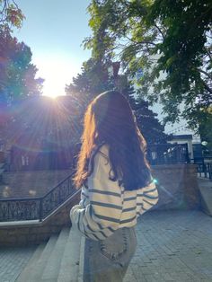 a woman walking down some steps towards the sun shining on her face and back,