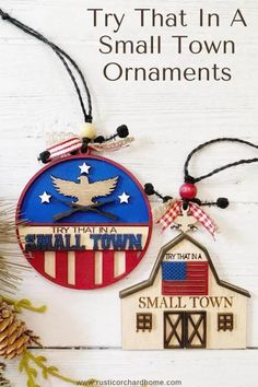 two small town ornaments are hanging on a white wooden background with pine cones