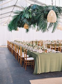 an indoor tent with tables and chairs set up for a formal dinner or party, surrounded by greenery