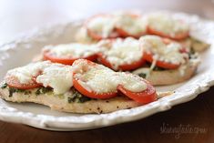 two small pizzas with tomatoes and cheese on them sitting on a white paper plate