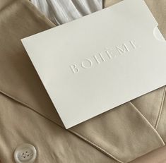 a white piece of paper sitting on top of a beige jacket with the word boheme printed on it