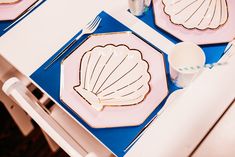 two plates with seashells on them are sitting on a blue and pink table