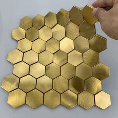 gold hexagon tiles are being painted on the wall by someone's hand