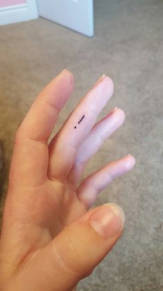 someone is holding their hand up to show the tiny finger tattoo on their thumbnail