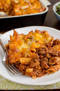 a white plate topped with lasagna covered in ground beef and cheese next to a bowl of salad