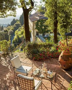 an outdoor patio with chairs, table and potted plants on the ground in front of trees