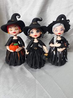 three little dolls dressed up as witches on a white sheet with a pumpkin in their hand